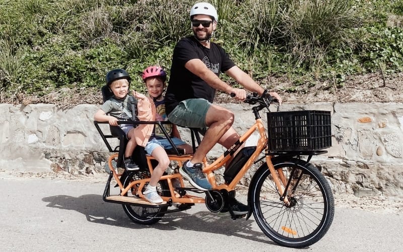 A rider on a Tribe Evamos Longtail with two children on the rear rack